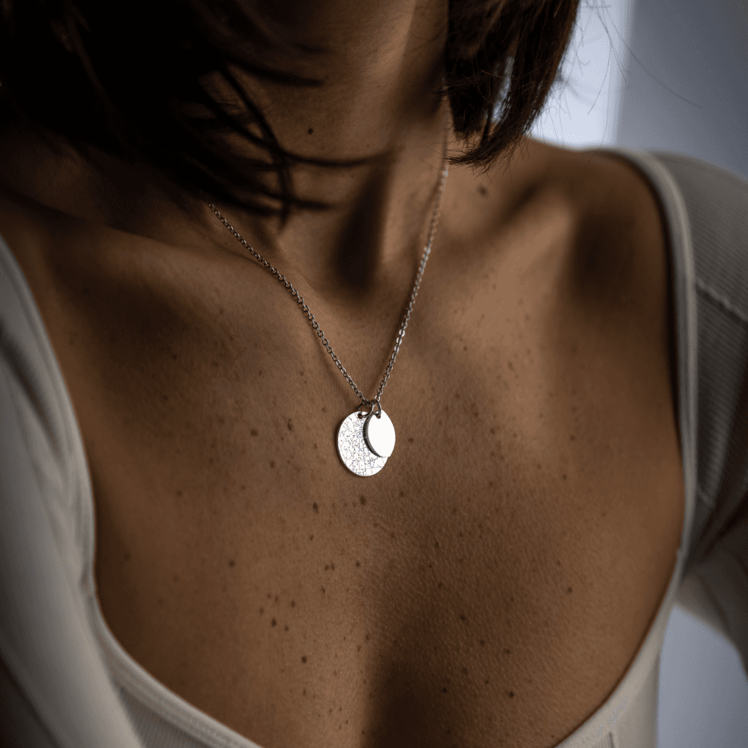 A woman wearing a three-quarter silver Night Sky Moon Phase pendant layered on top of a bigger Night Sky Star Map Silver pendant.