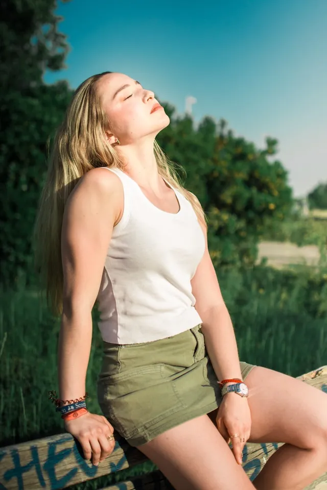 Woman in a white top standing outdoors in warm natural light, looking upward