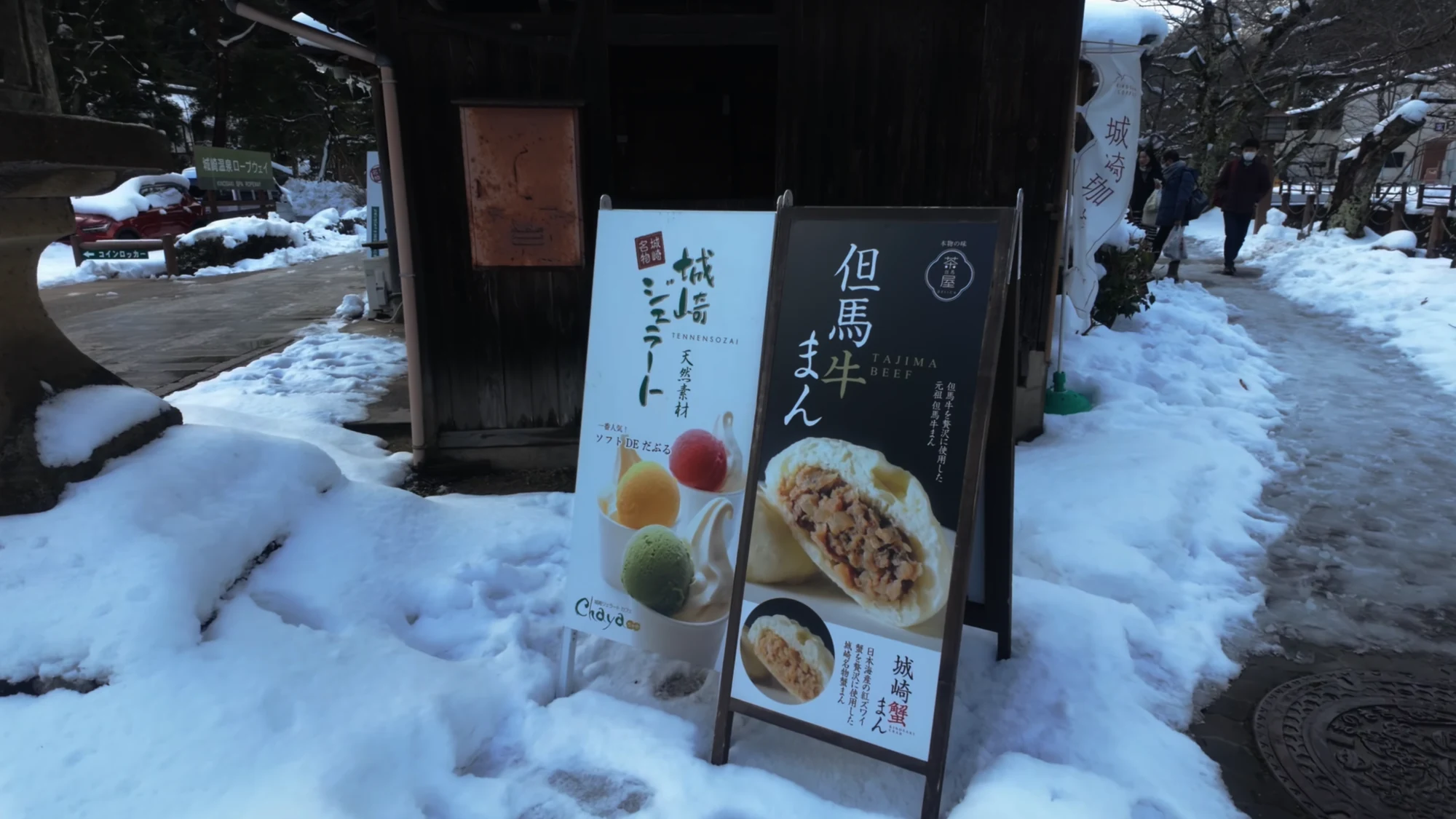 A Tajima beef shop board standing in snow on a Kinosaki street.
