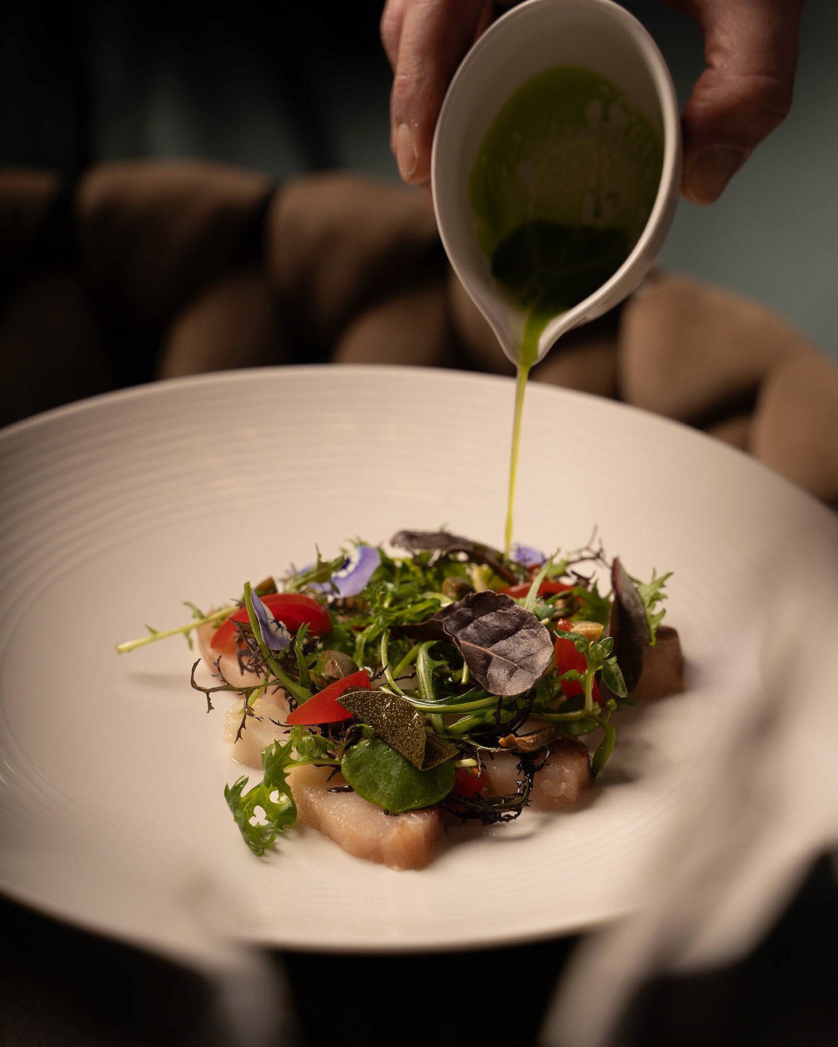 „Fein angerichteter Teller mit frischem Fisch-Carpaccio, buntem Blattsalat, Kräutern und essbaren Blüten, übergossen mit einem grünen Kräuteröl.“