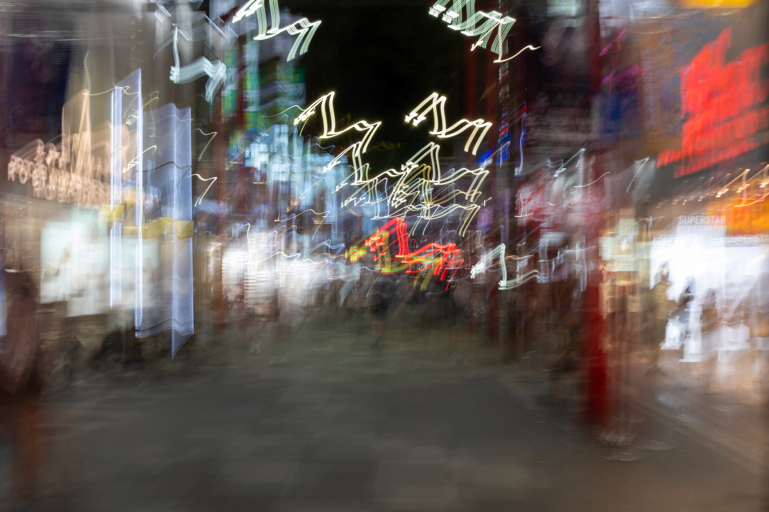 Color abstract motion blur photograph of people walking through a busy shopping street with bright neon lights streaking through the scene.
