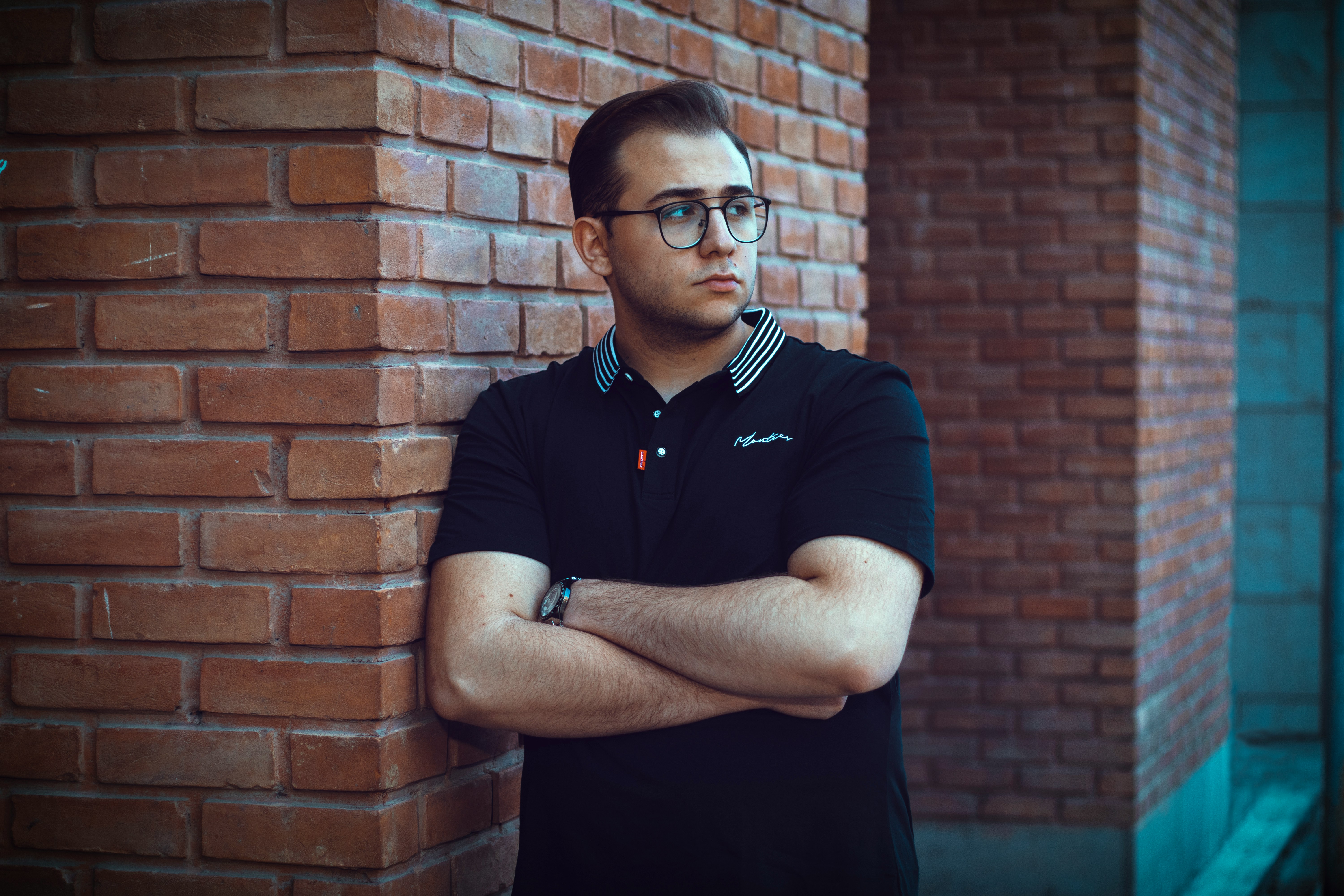 a man leaning against a brick wall with his arms crossed
