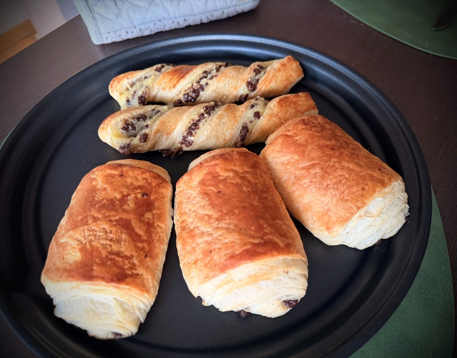 Three pains au chocolat and two twisted chocolate pastries on a dark plate.