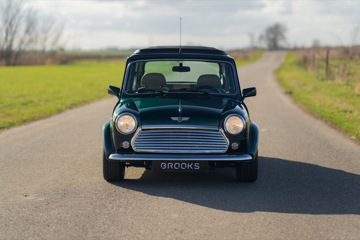 A black vintage car parked on a curved road surrounded by green fields under a bright sky.