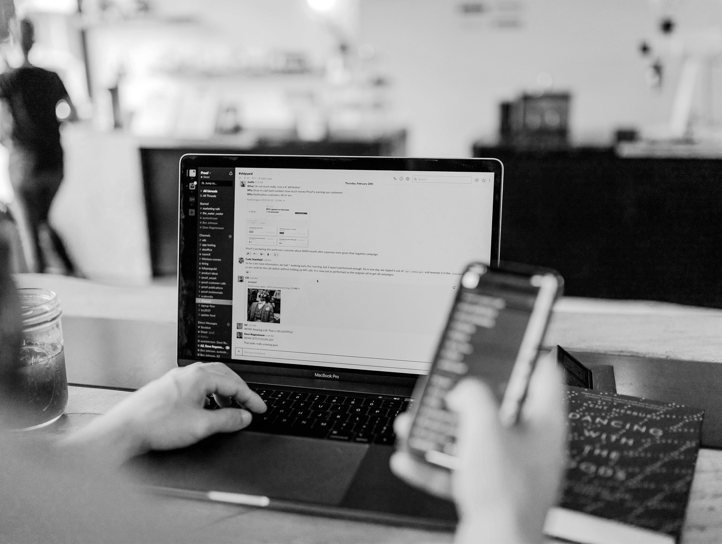 A person uses a smartphone while working on a laptop in a modern, minimalistic workspace.