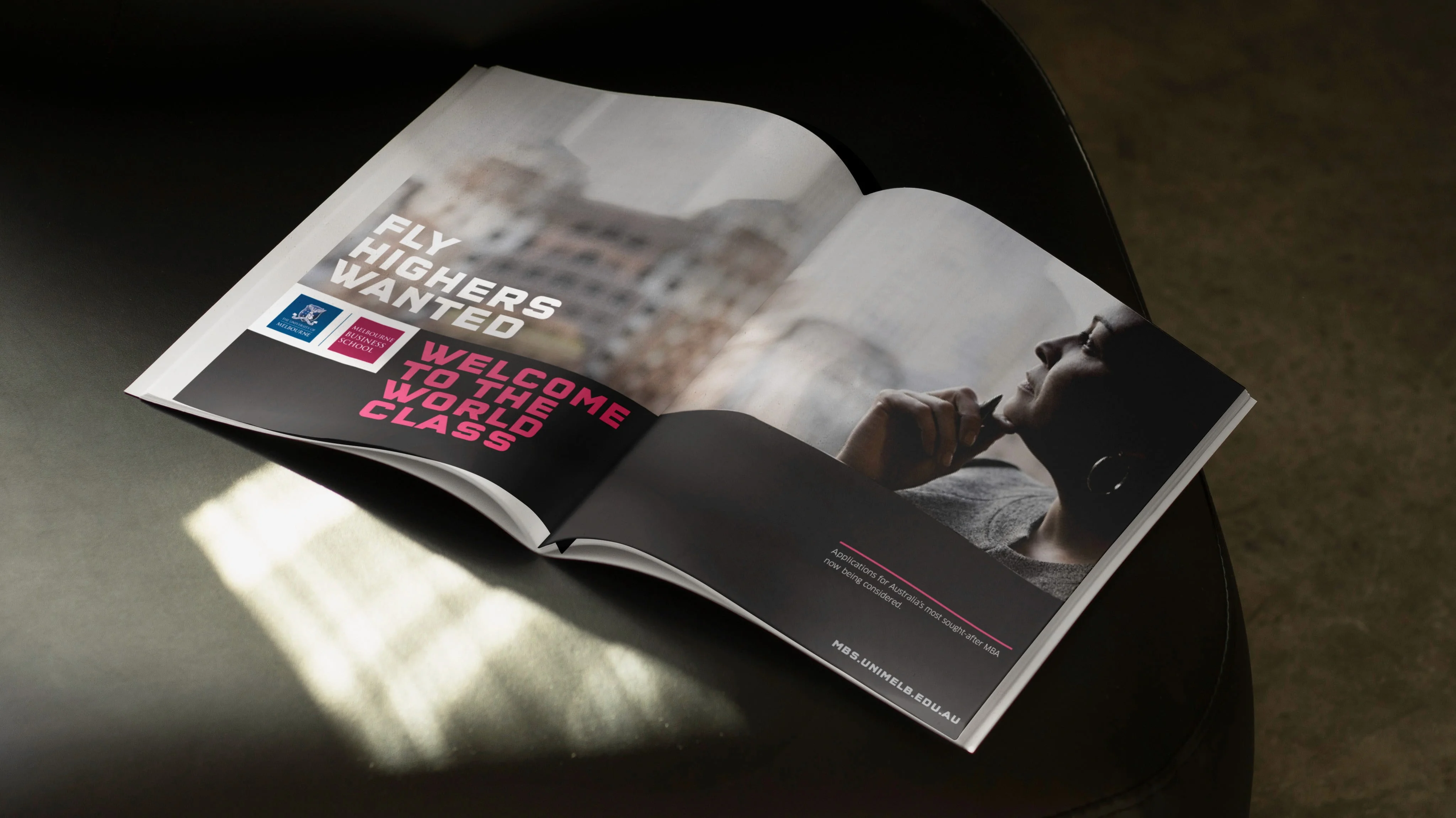 Melbourne Business School magazine ad on a table: 'Fly highers wanted. Welcome to the world class.' beside a thoughtful woman