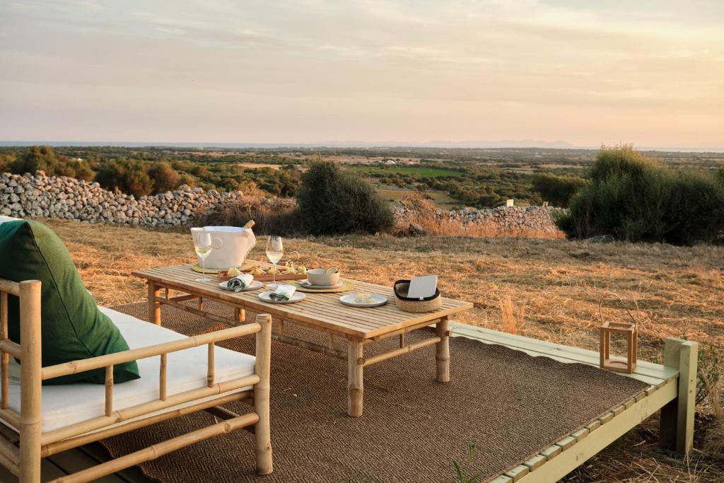 Outdoor restaurant terrace overlooking a tranquil lake at sunset. White tables and chairs are set with glassware. Sheer curtains add elegance. Calm ambiance.