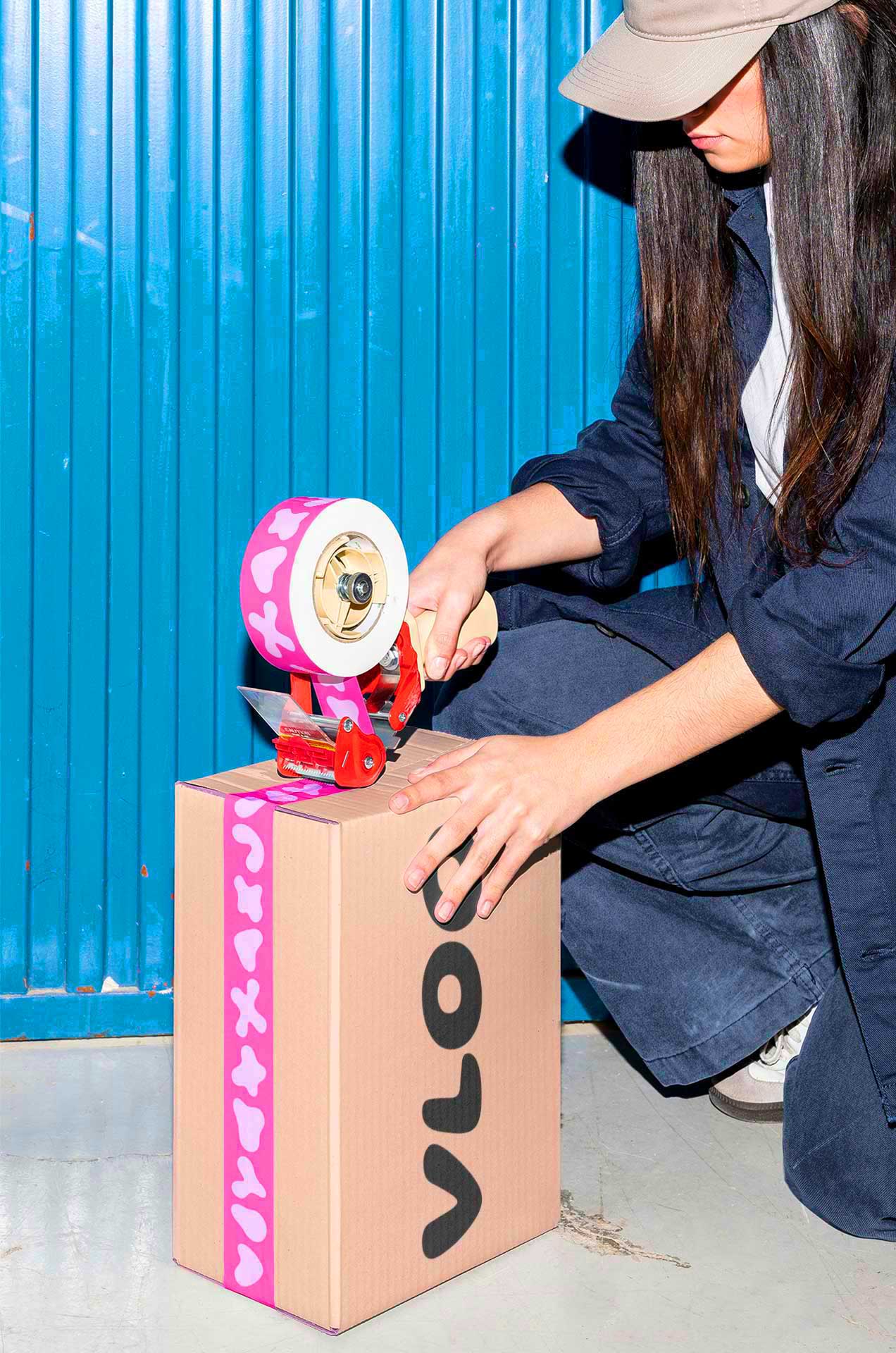 A woman kneeling down to tape up a VLOO subscription box with hot pink tape with VLOO's organic shapes.