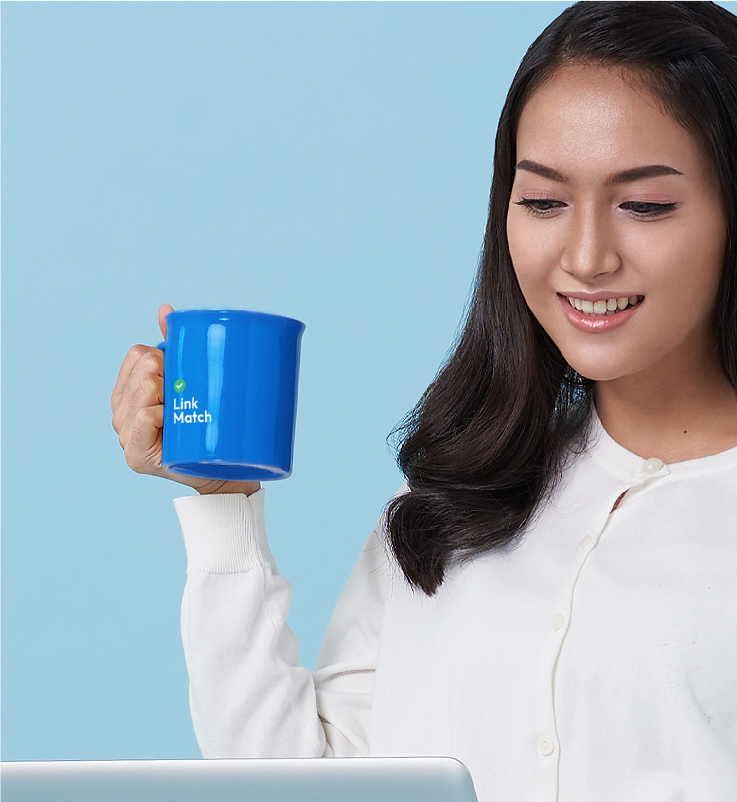 Person holding a blue LinkMatch branded mug while working on a laptop