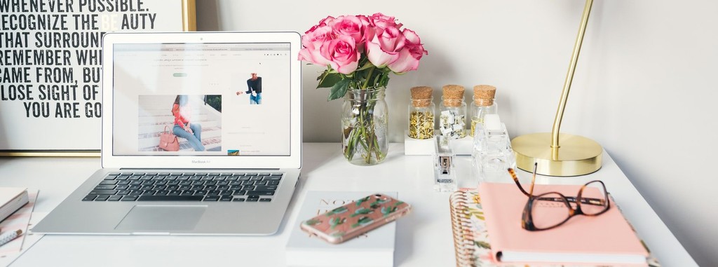 Modern home office desk with laptop, pink roses, and notebooks.