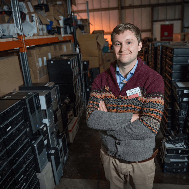 Photo of the founder of the Turing Trust standing arms folded and smiling in the triusts wharehouse