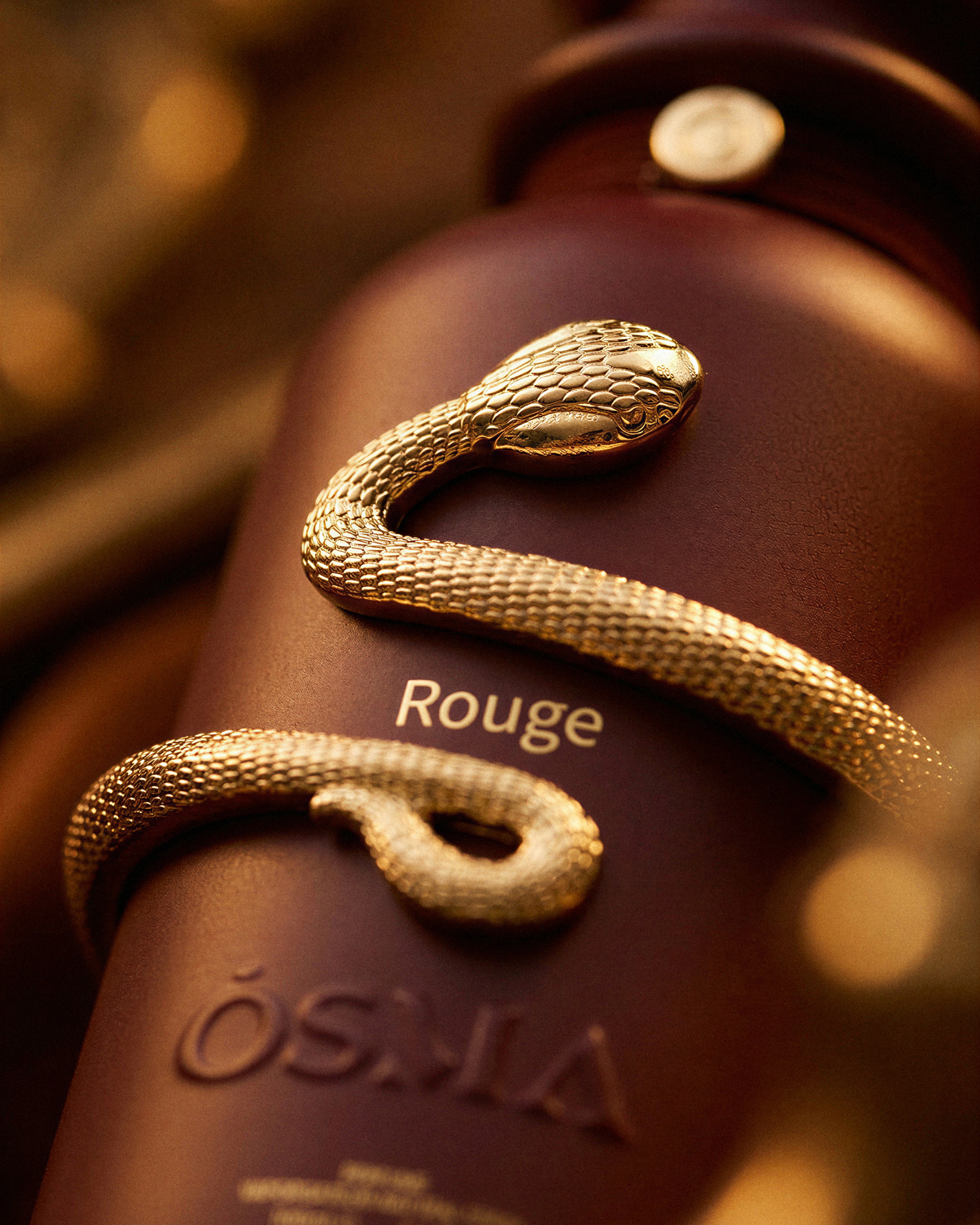 Gold serpent detail wrapped around a deep red ÓSMA Rouge fragrance bottle