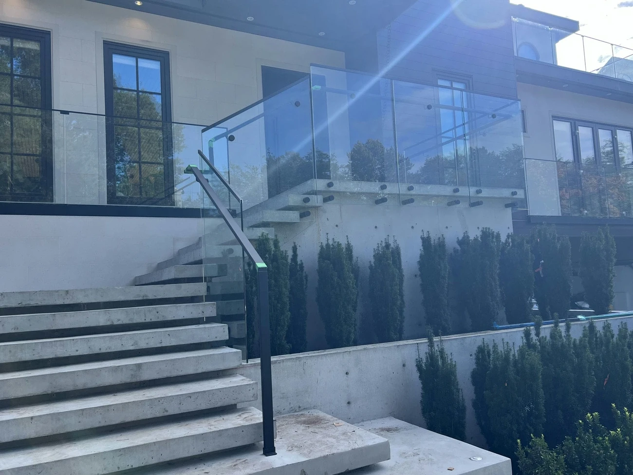 Modern concrete stairs with sleek glass railings and balustrades in front of a contemporary building with large windows.