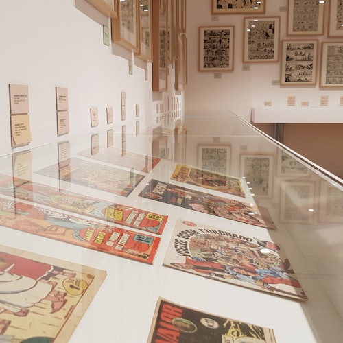 在灯光明亮的展览厅内,漫画书被陈列在玻璃展柜中,墙上挂有装裱好的漫画页面和描述。