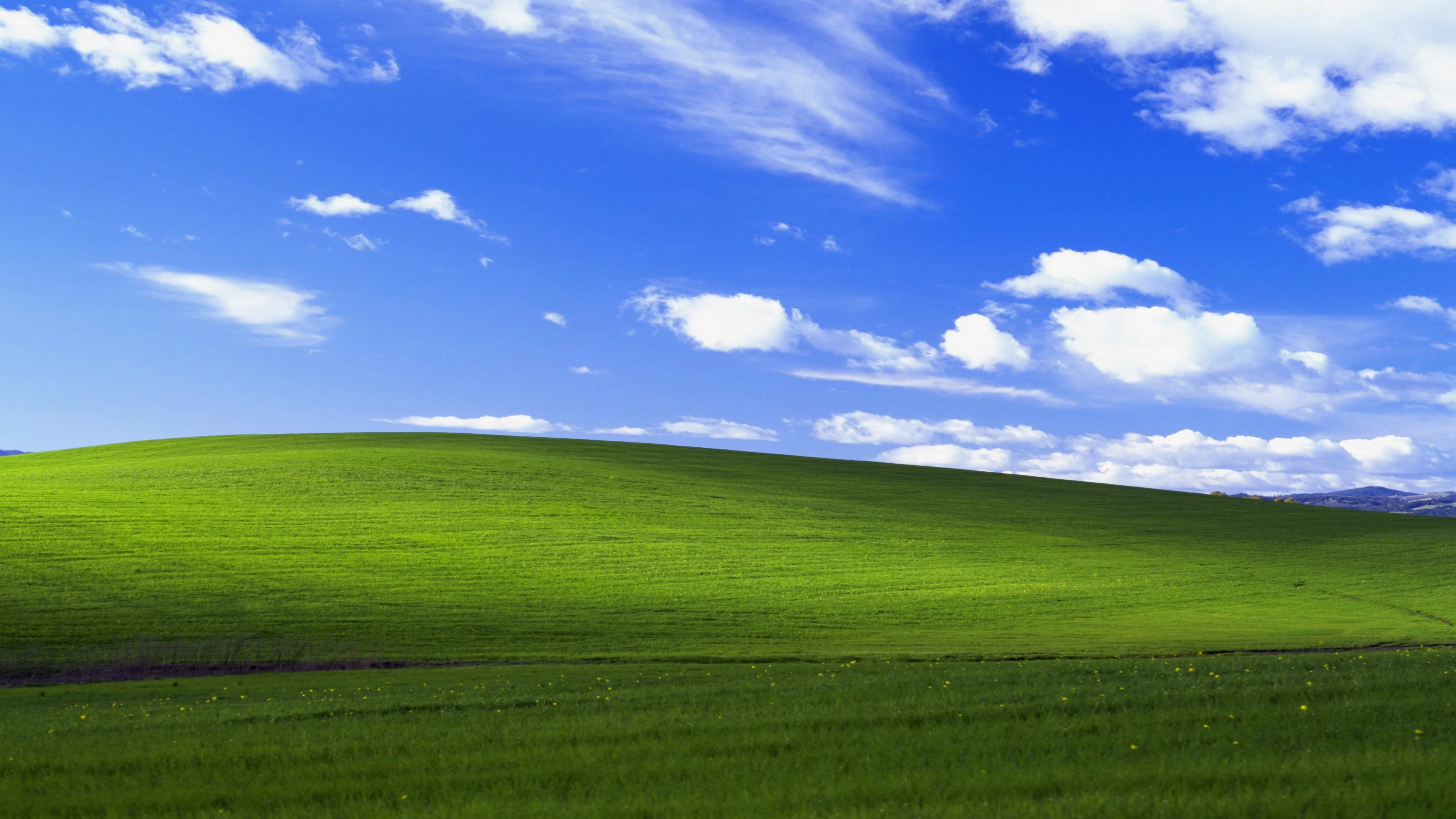 Blue sky with white clouds over a green rolling landscape, in the spirit of the Windows XP Bliss wallpaper