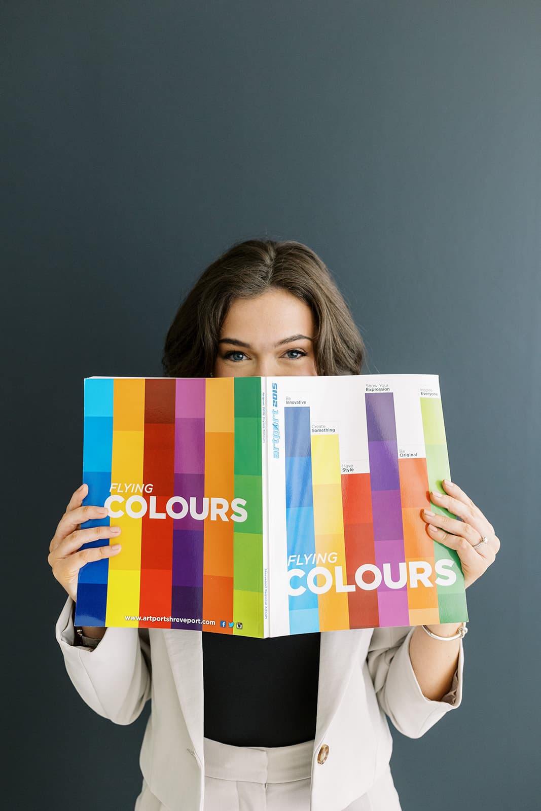 A model playfully holds up a colorful book while posing at Revelator Studio in Shreveport, captured by photographer Andy Roberts, highlighting the studio’s natural light and creative setting.