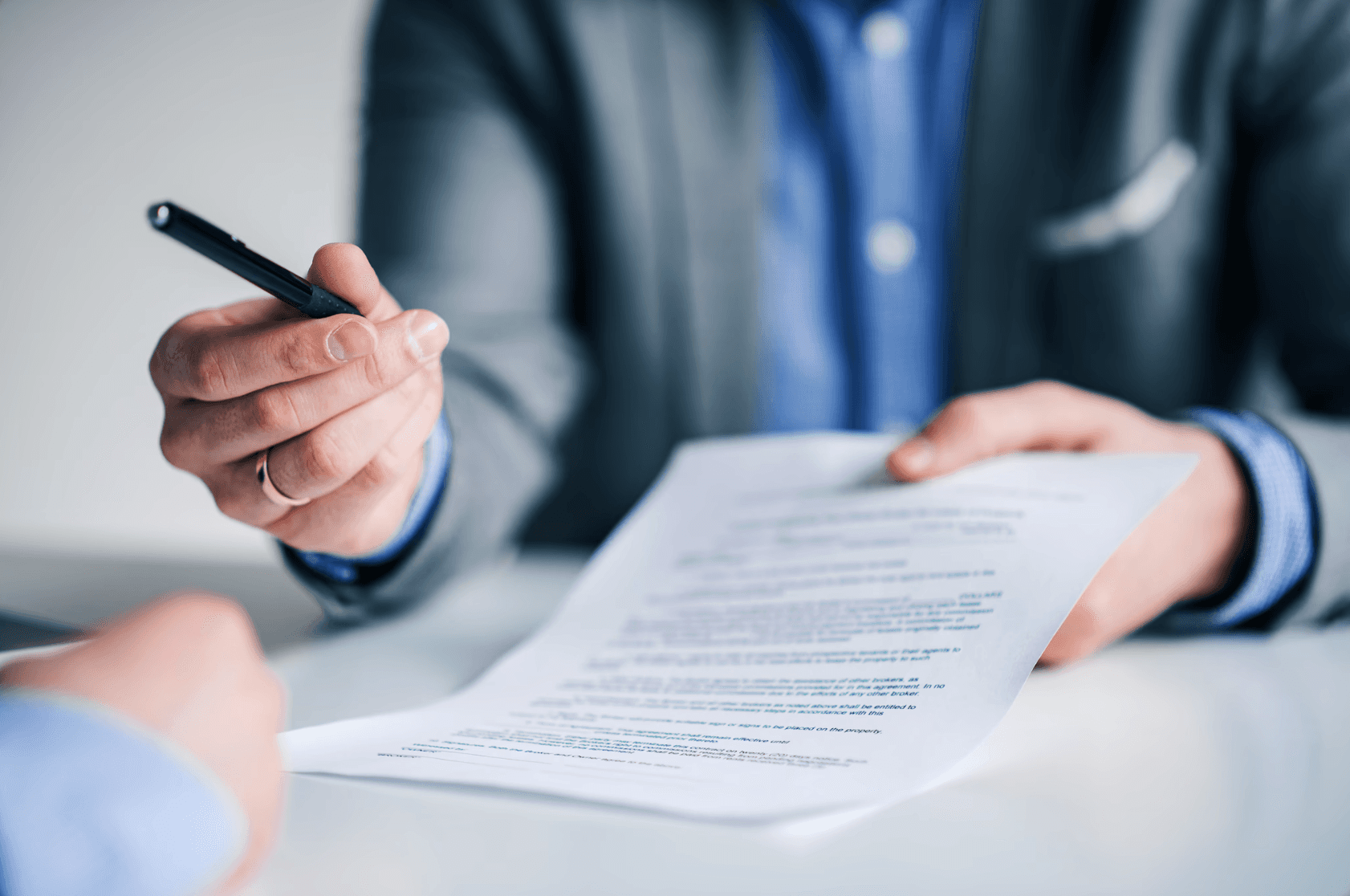 Pessoa vestindo terno entrega um contrato enquanto aponta com uma caneta, simbolizando a elaboração e revisão de contratos para proteção jurídica.