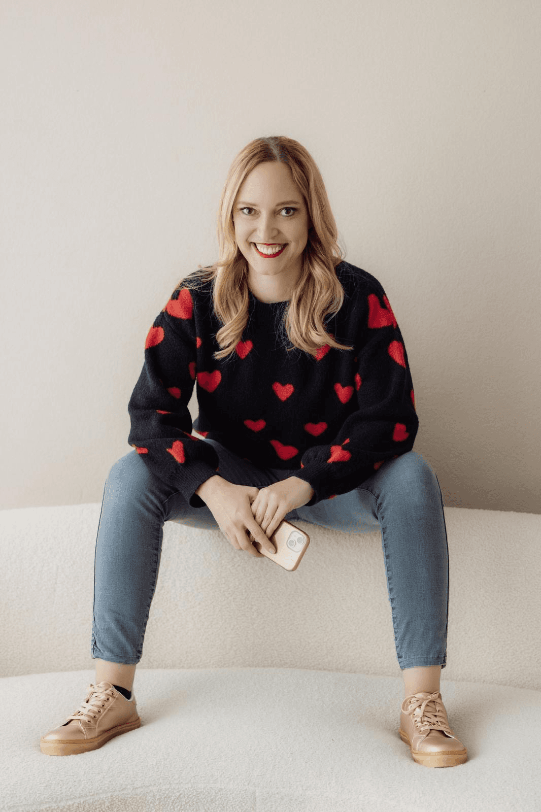 Simone Herzog seated on a white sofa wearing a black sweater with red hearts.