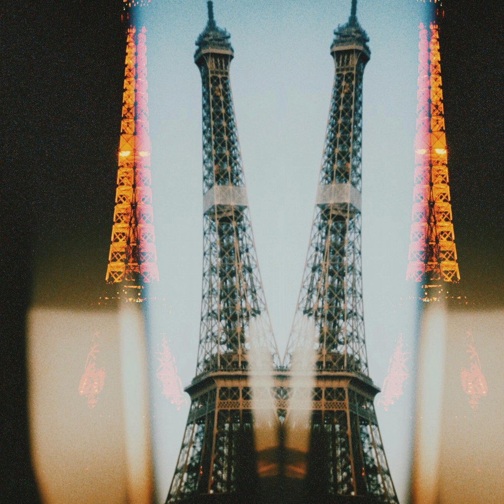 A creative, double-exposure photograph of the Eiffel Tower, blending two images to create a mirrored effect, with warm lighting accents that add a surreal and artistic touch to the iconic Parisian landmark.