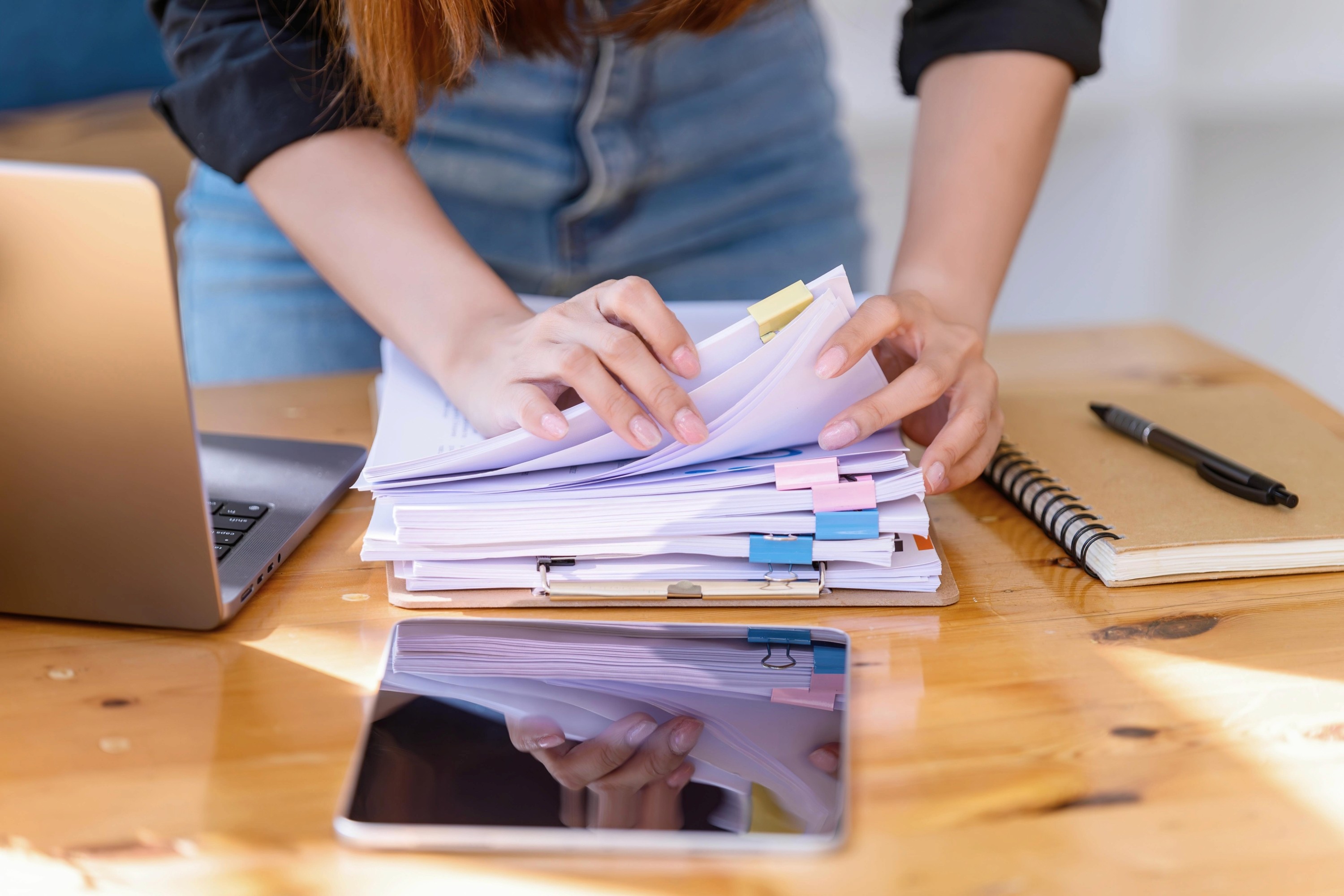 A person's hands reviewing papers and documents on a desk with a laptop, representing supplier or workforce management