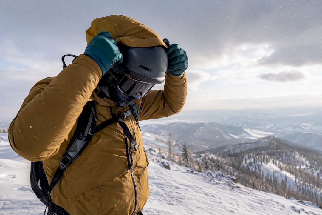 Traveller adjusting winter clothing layers on a snowy ridge