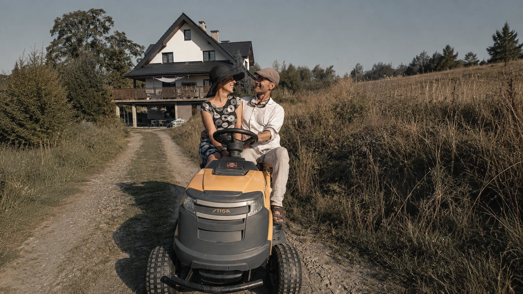 Zdjęcie właścicieli Powidoku podczas koszenia trawy przed domem w Wetlinie, na tle budynku i bieszczadzkiego krajobrazu.