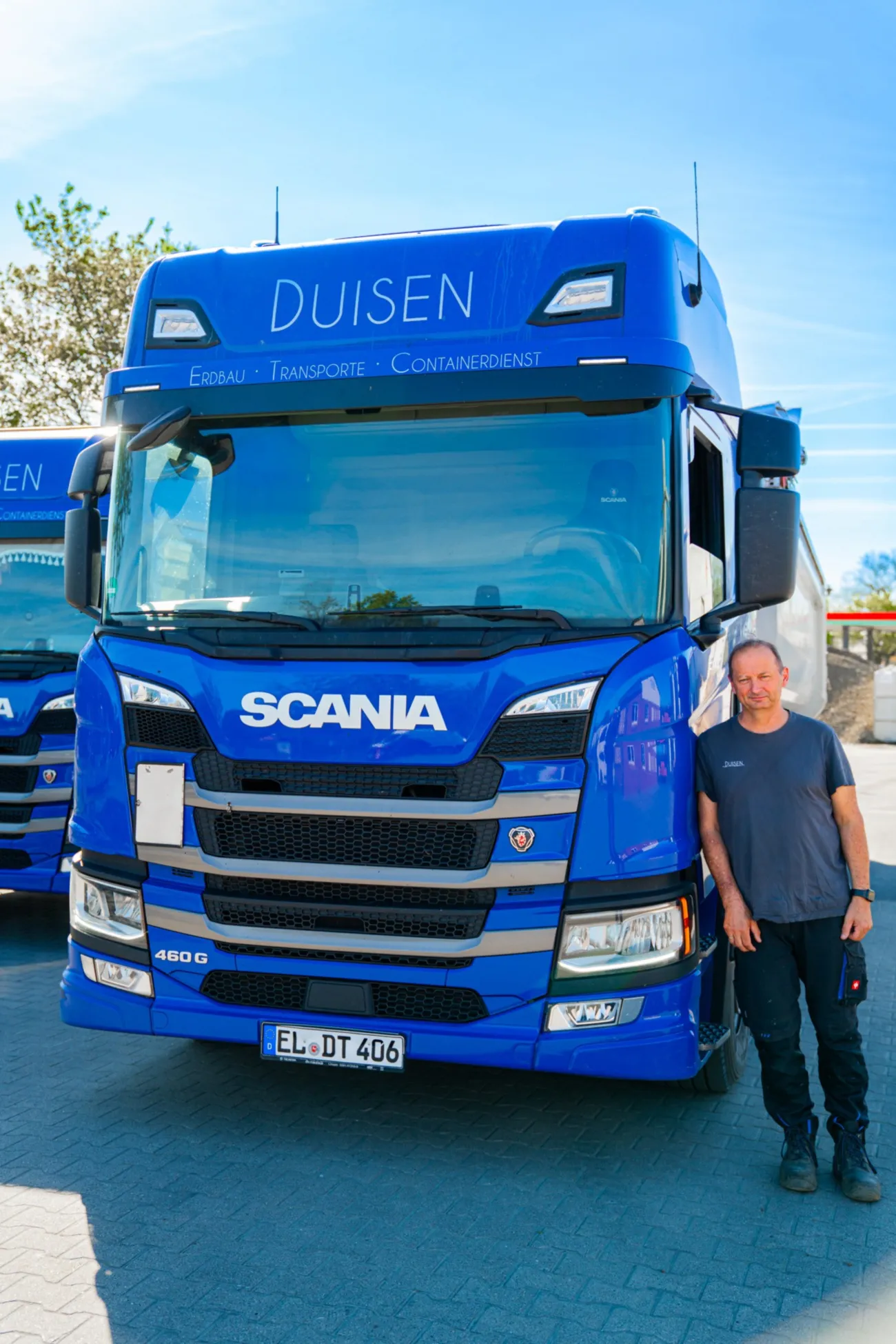 Blauer Scania-Lkw „Duisen“ mit Mitarbeiter davor auf dem Betriebshof
