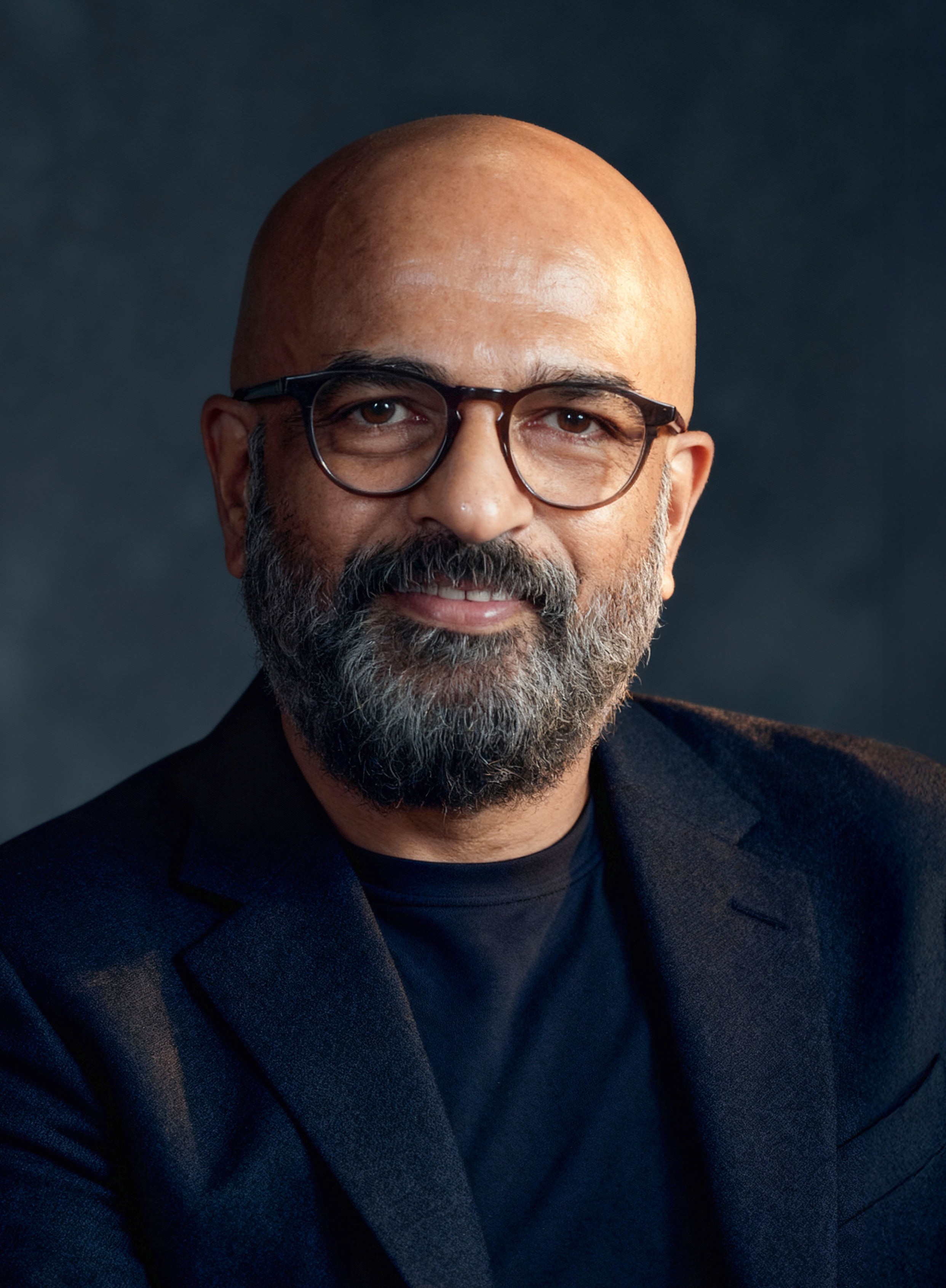 A woman with curly hair, wearing round glasses and a white t-shirt, smiling gently.
