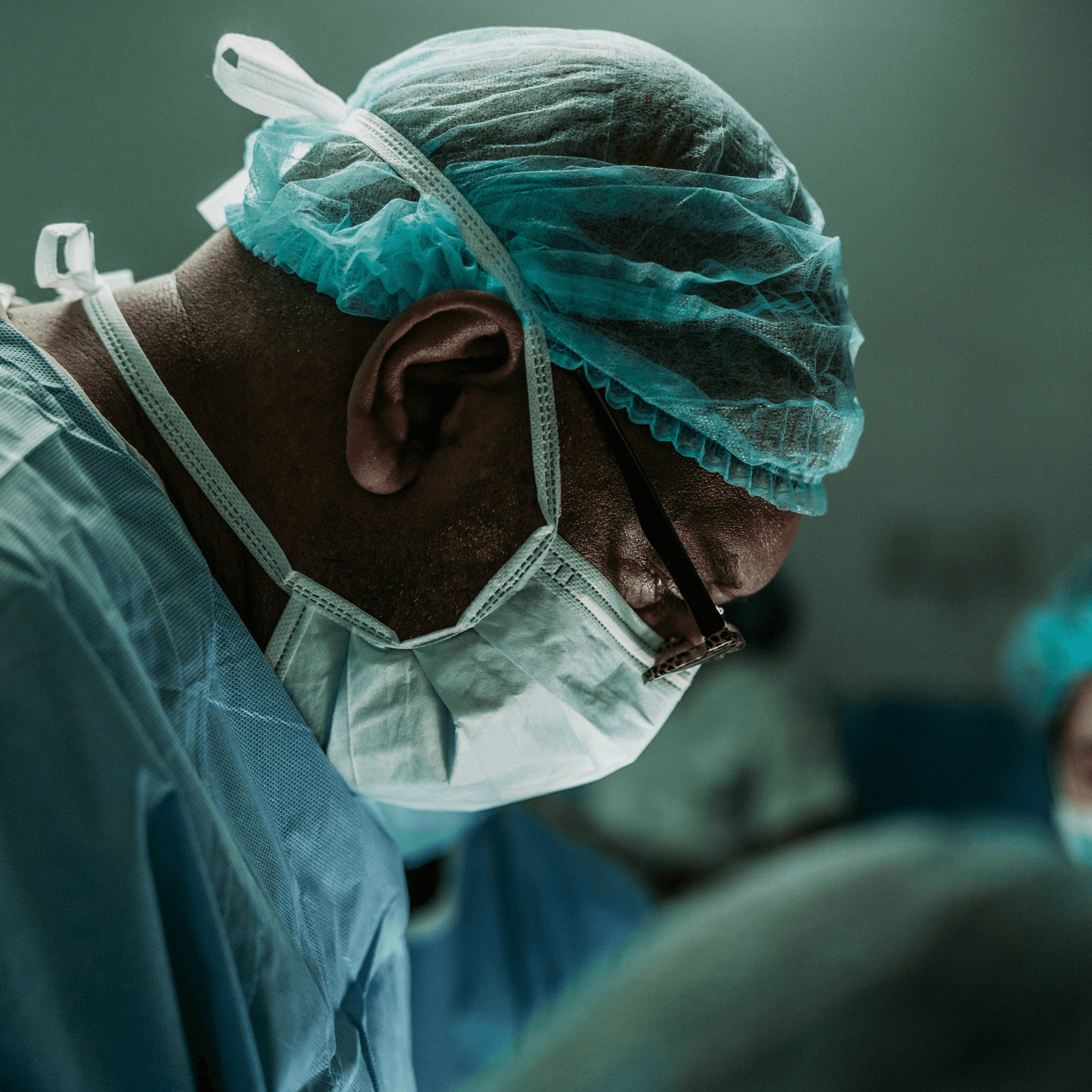 An anesthesia provider in surgical cap and mask focused during a clinical procedure in an operating room