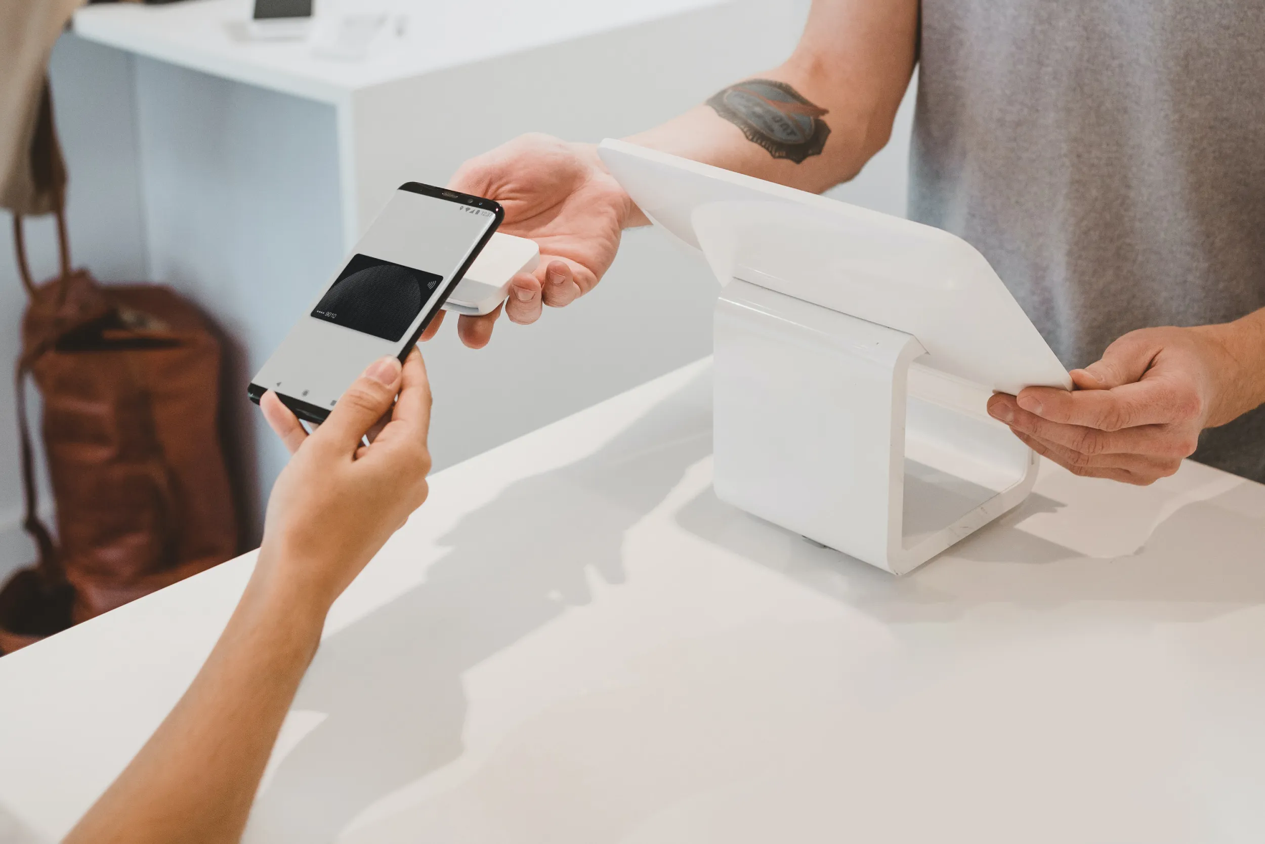 A person using a phone to tap at a payment point held by a store clerk who is also standing in front of a tablet.