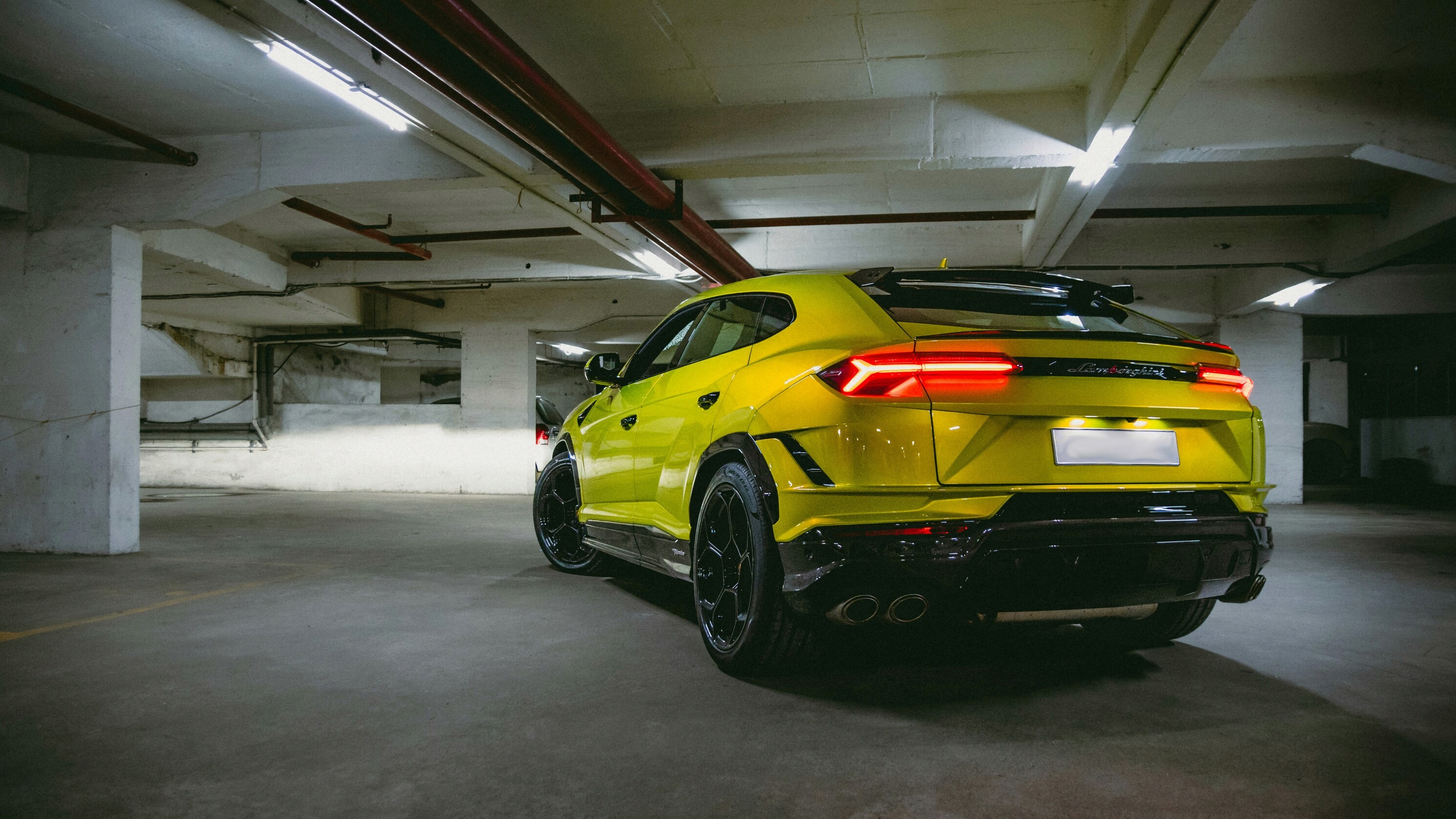 Rear view of a yellow Lamborghini Urus SUV parked. Black rims, taillights, and spoiler are visible. 