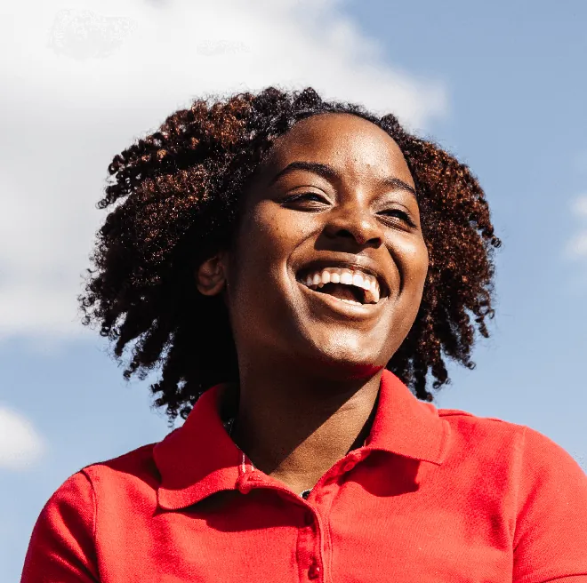 Woman in a red polo laughing against a blue sky.