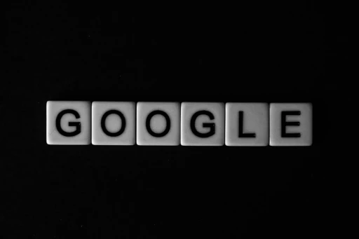 Black-and-white image of tiles spelling “Google” on a dark background.