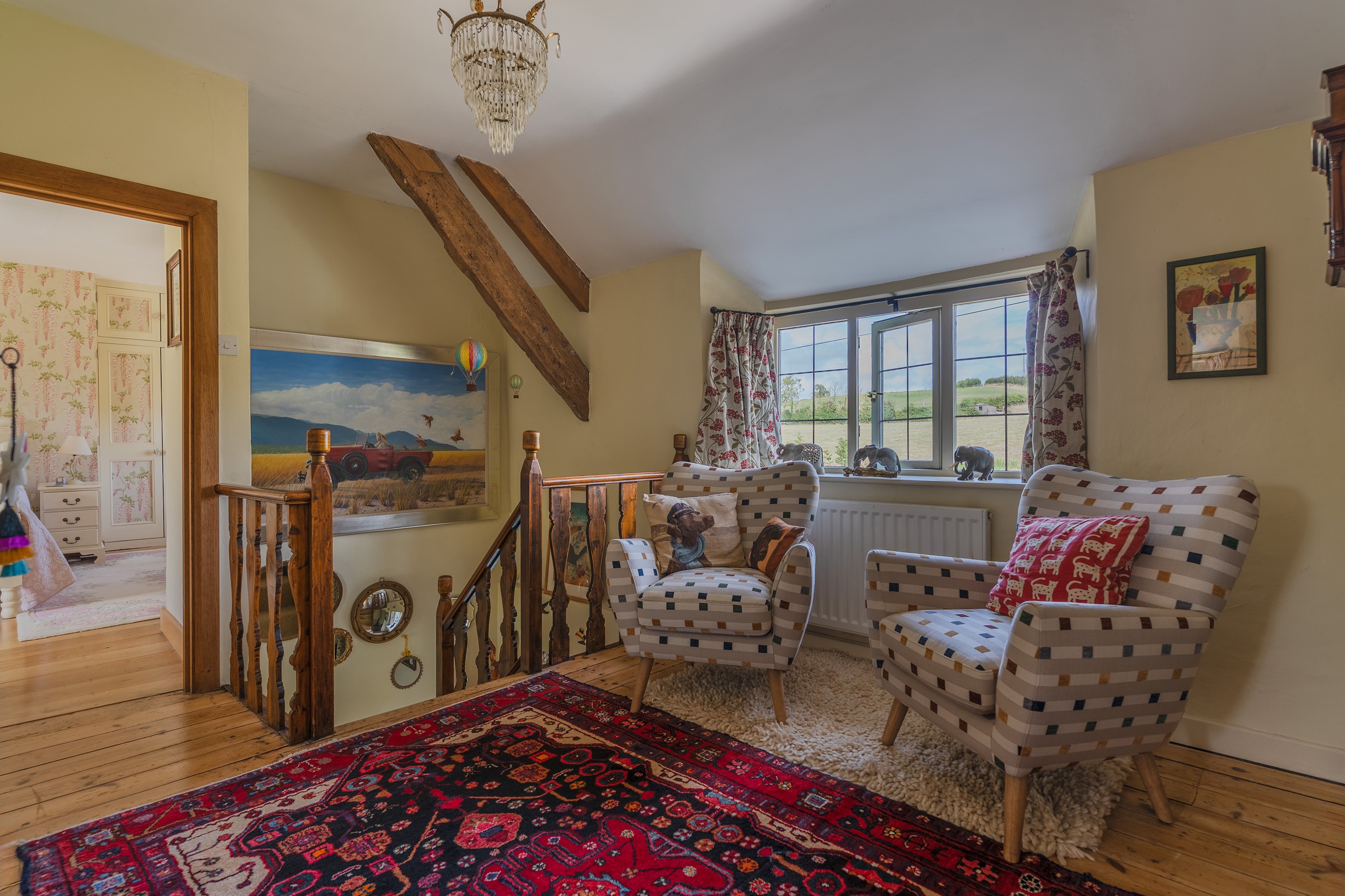 Landing at Box Cottage with exposed beams and two armchairs beside a leaded window looking out over fields, Launcherley, near Wells — Captura Media