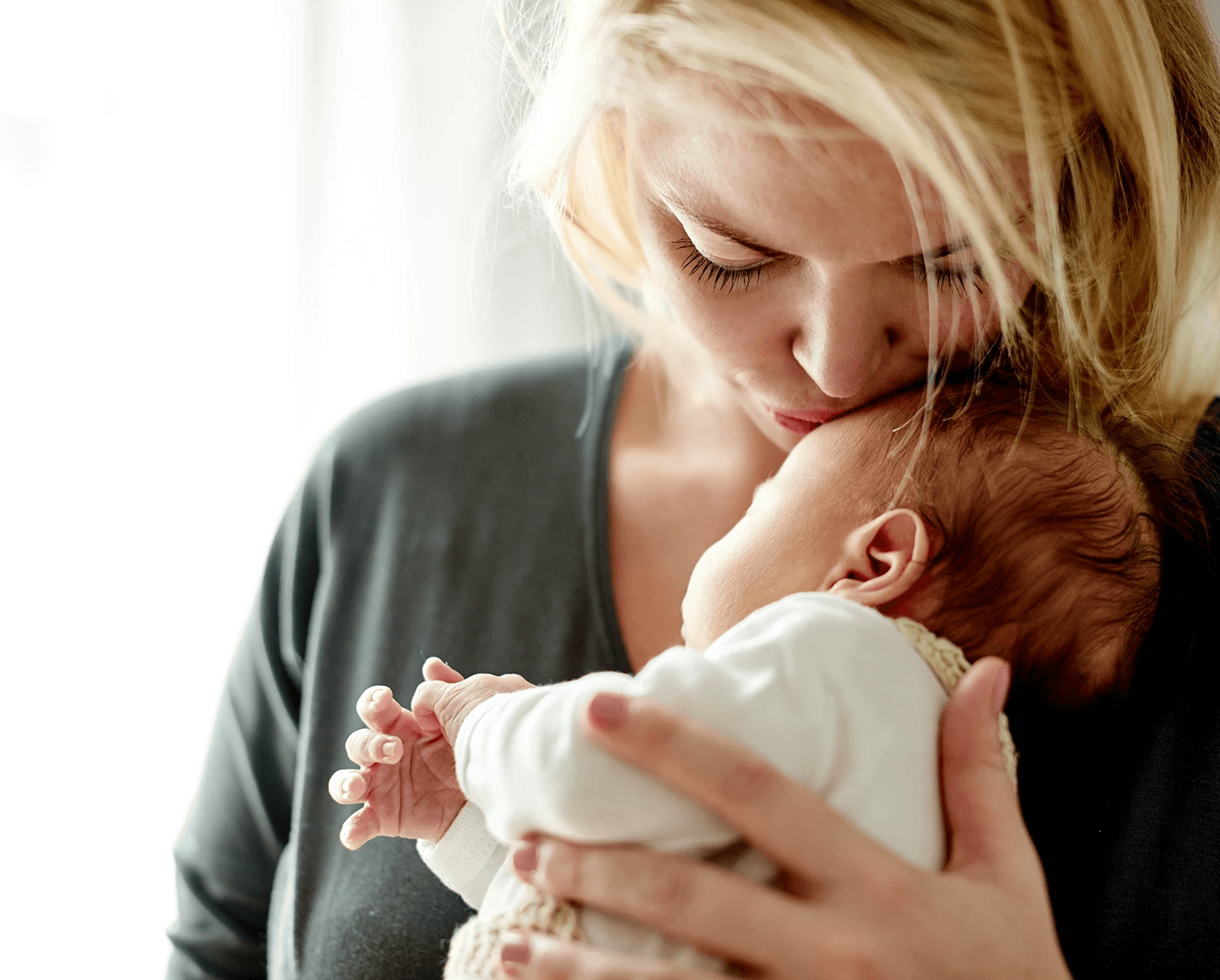 Woman kissing the head of her baby representing Postpartum care