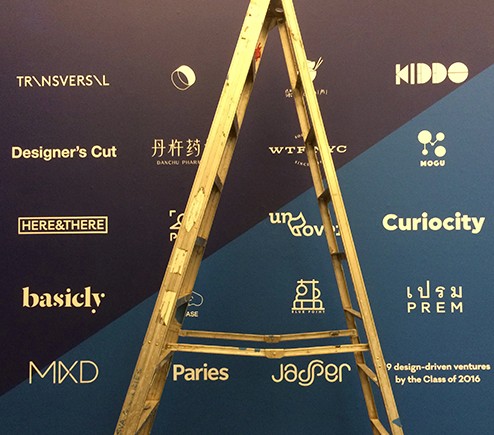 A photo of a metallic golden ladder in front of a black, blue and yellow logo poster on a wall.