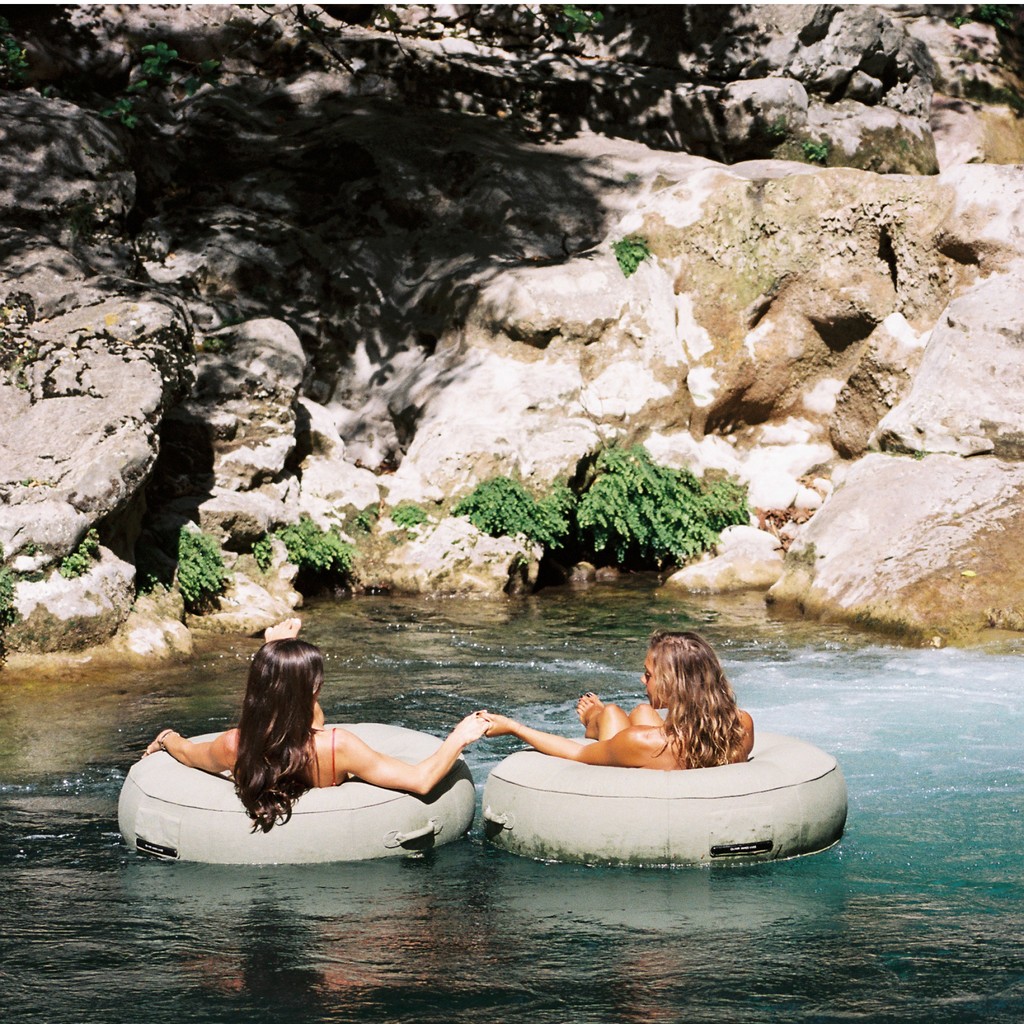 Two women floating on luxury green pool floats in a natural rock pool surrounded by sunlit cliffs