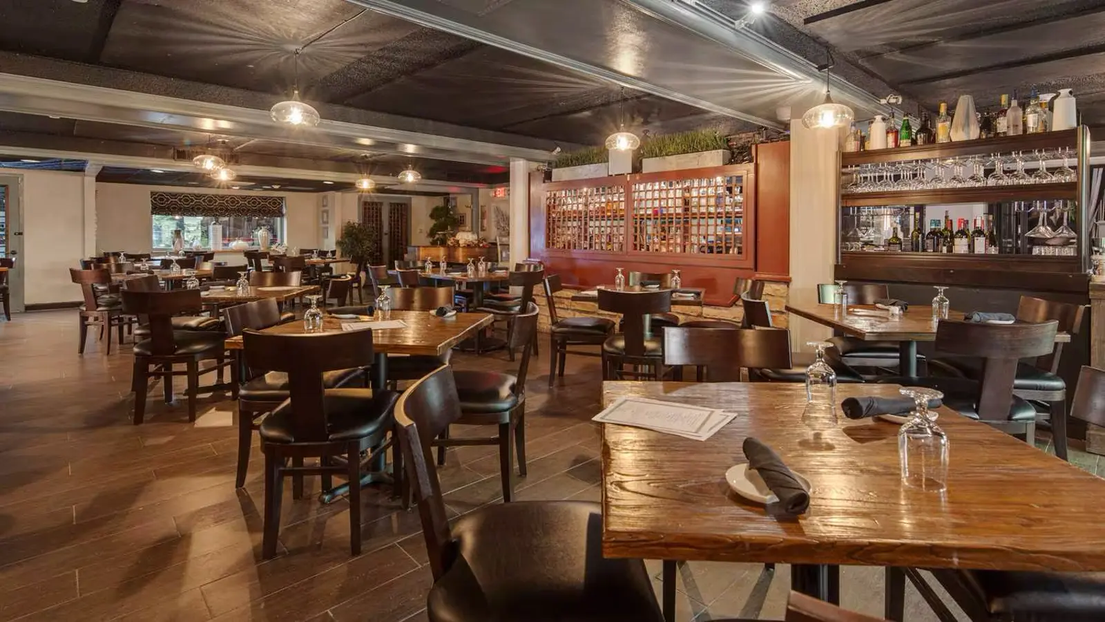 Restaurant dining room with many set tables, chairs, and a bar.