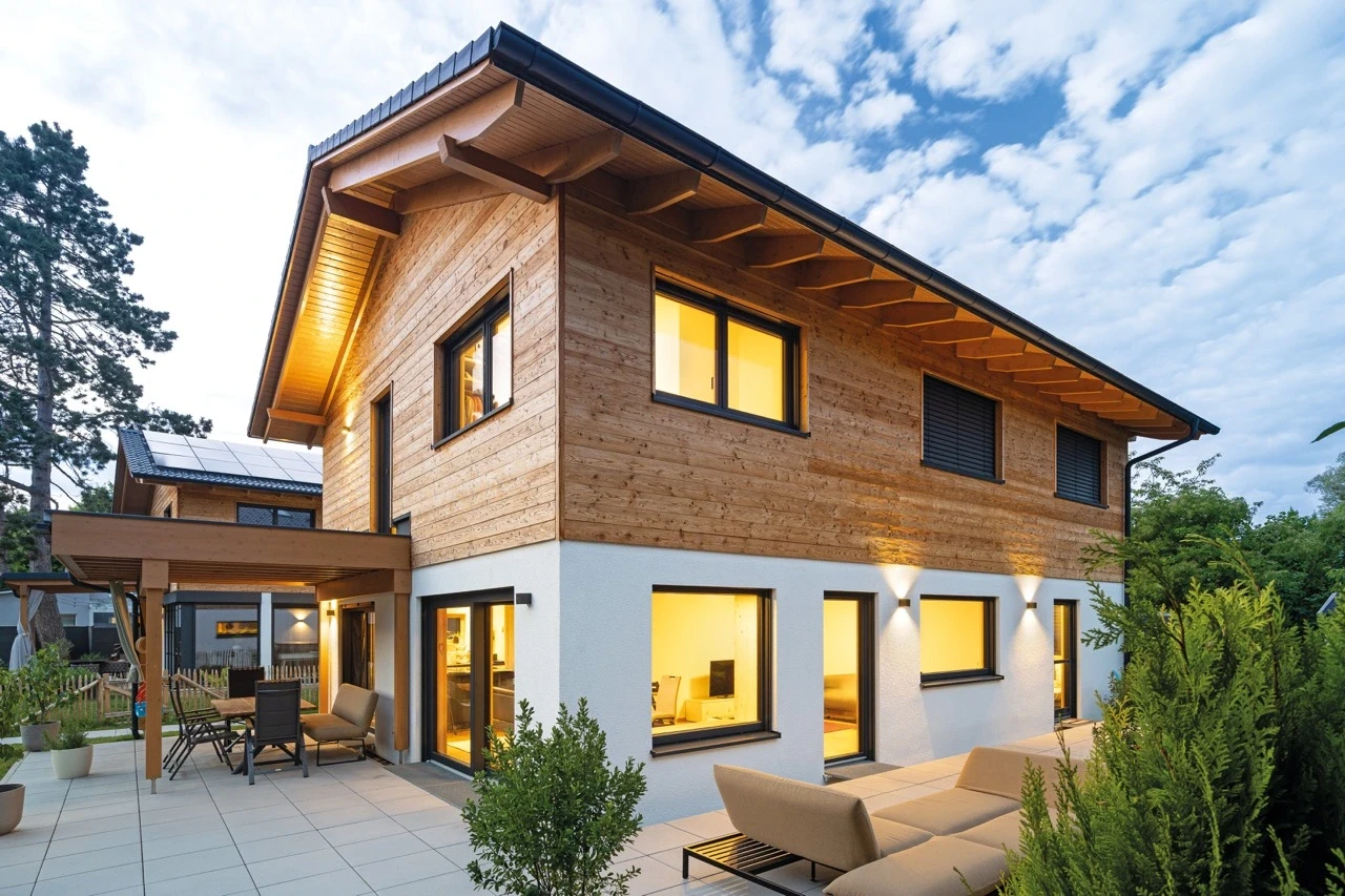 Modern two-story wooden house with large windows and outdoor seating.