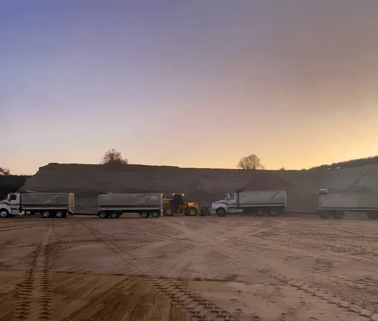 Two trucks and loader in a sand quarry at sun rise