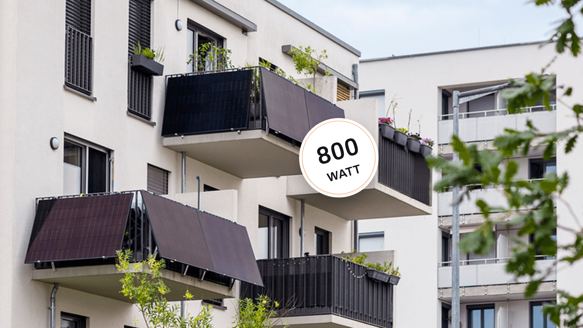 Modernes Wohngebäude mit mehreren Balkonen mit Photovoltaikmodulen und Grünflächen im Vordergrund.