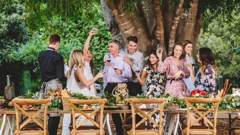 Guests celebrating under a fig tree at an outdoor lunch table setting