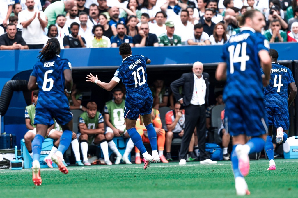Kylian Mbappé leaps in celebration as France teammates surge toward the dugout against Iraq