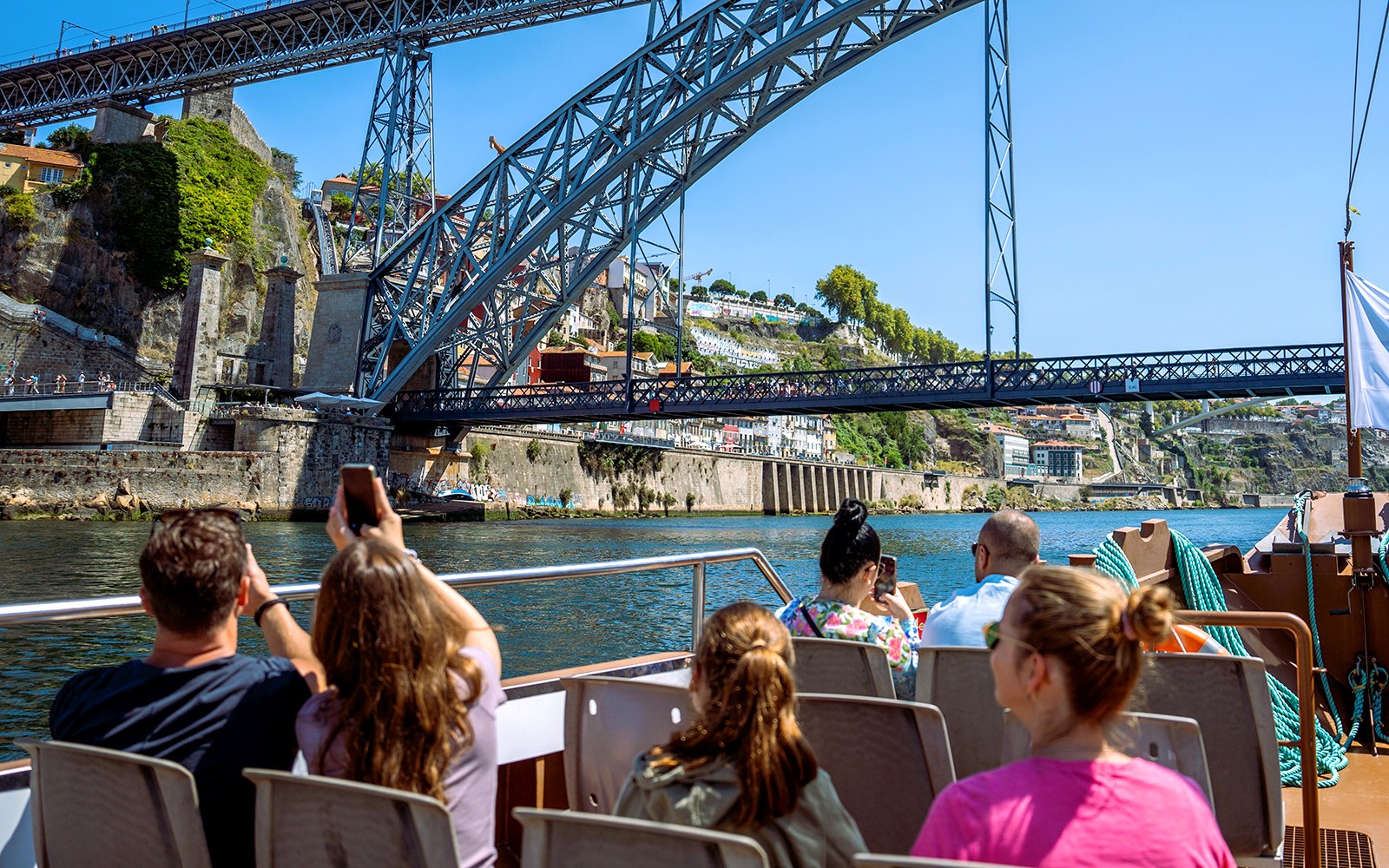 游客们在葡萄牙波尔图的Dom路易士一世大桥下乘船游览,拍摄城市的美景。