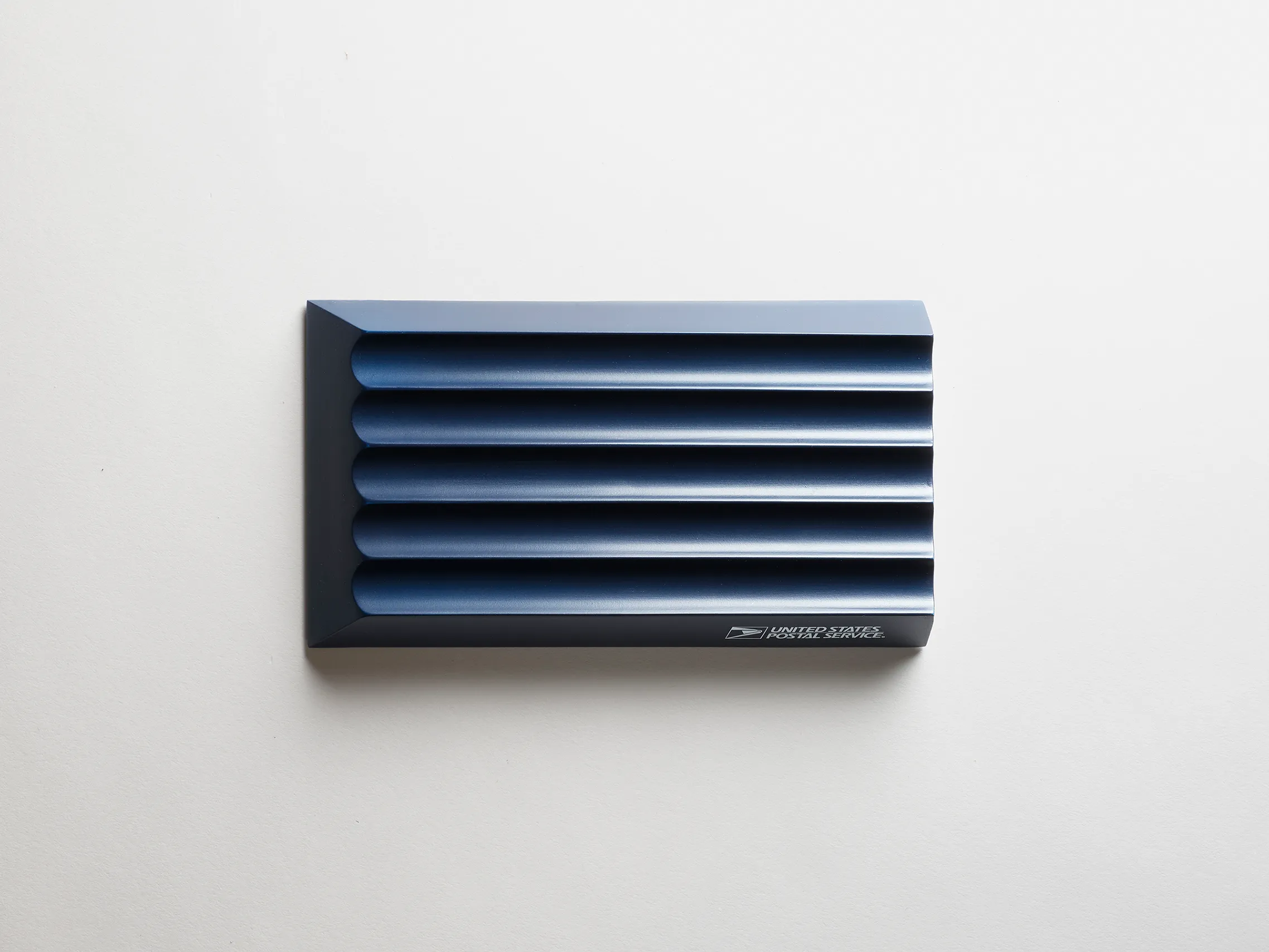 Dark blue USPS mailbox sensor with horizontal slats on a white background