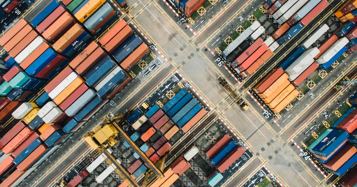 Aerial view of a busy container terminal with rows of colorful shipping containers, cranes, and marked freight lanes.
