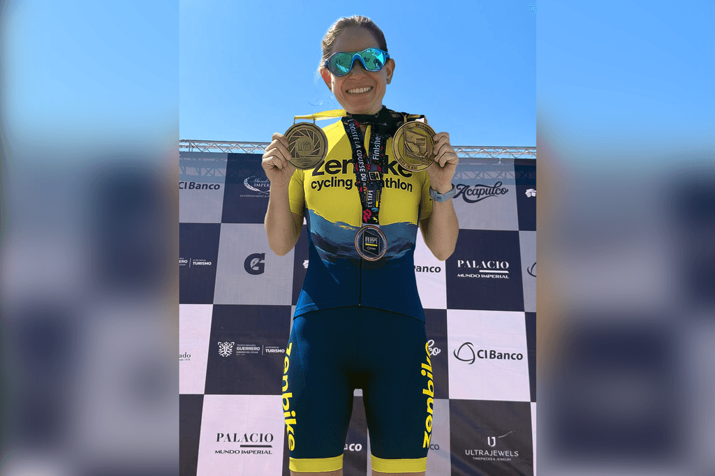 Ciclista en el podio mostrando medallas de primer lugar nacional y sonriendo.
