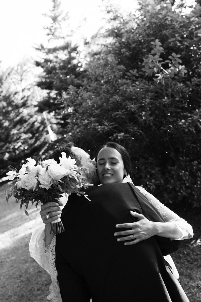Sposi si abbracciano nel parco, lei con bouquet di peonie bianche, reportage di matrimonio in bianco e nero