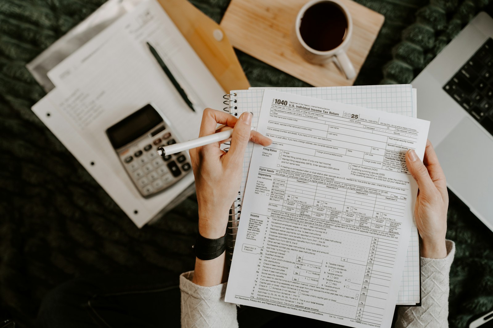 Hands reviewing tax forms with a calculator and laptop