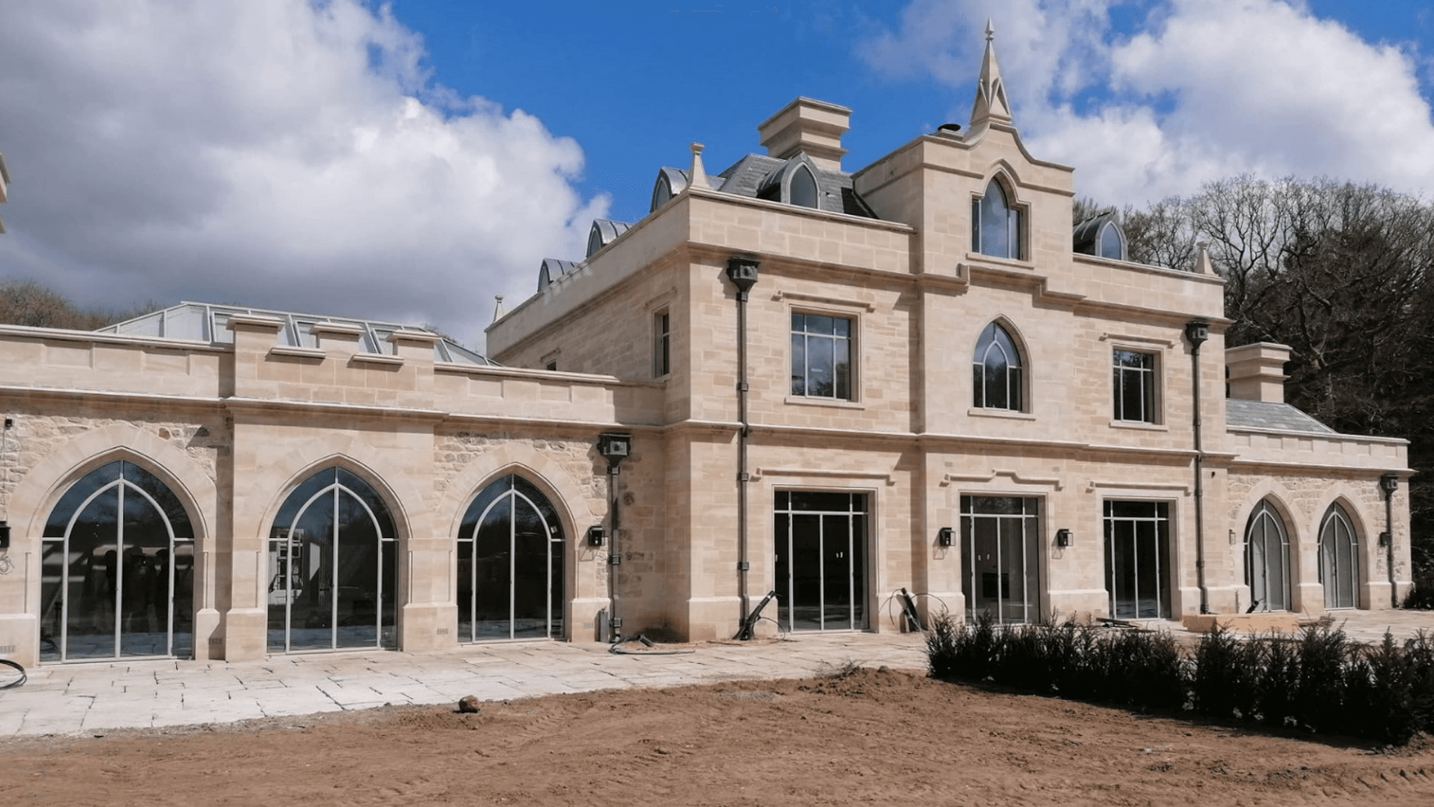 A grand, light-colored mansion with large arched windows, against a bright blue sky with clouds.